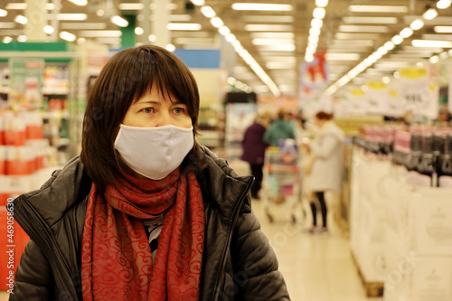 Woman in warm clothes and medical mask choosing products in a supermarket. Concept of safety during shopping at coronavirus pandemic © Oleg