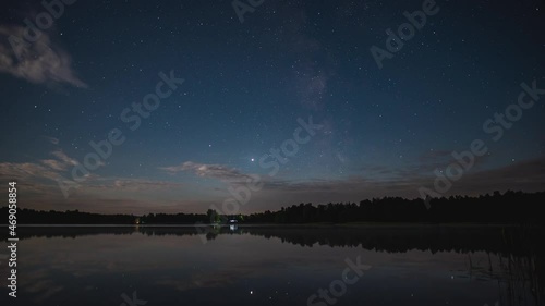 Timelapse of the movement of the starry sky with clouds over the lake on a summer night.