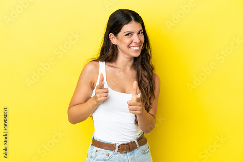 Young caucasian woman isolated on yellow background surprised and pointing front