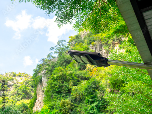 Solar light. Modern electrical power led light bulb hanging on the pole under the roof of building on green nature mountain and blue sky background.