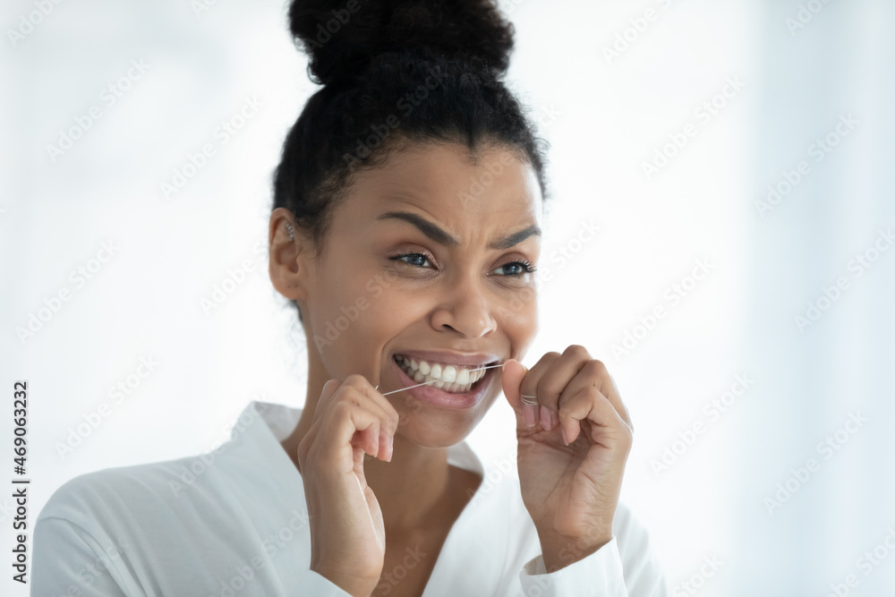 Mirror reflection happy young african ethnicity woman in bathrobe cleaning teeth with dental floss, involved in doing daily oral care routine in bathroom, preventing caries, teeth treatment concept. Mirror reflection happy young african ethnicity woman in bathrobe cleaning teeth with dental floss, involved in doing daily oral care routine in bathroom, preventing caries, teeth treatment concept.