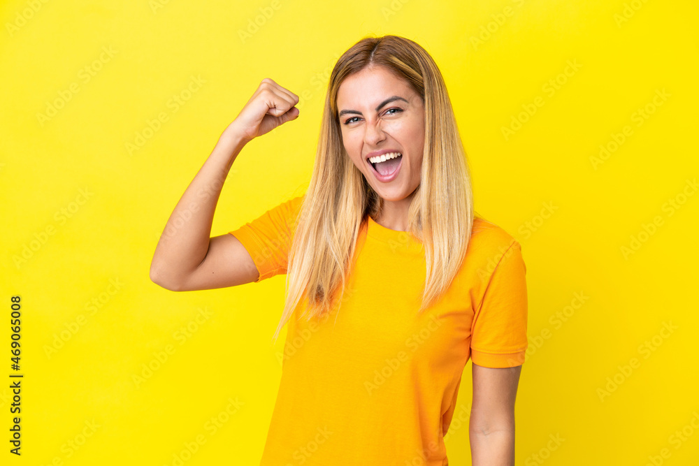 Blonde Uruguayan girl isolated on yellow background celebrating a victory