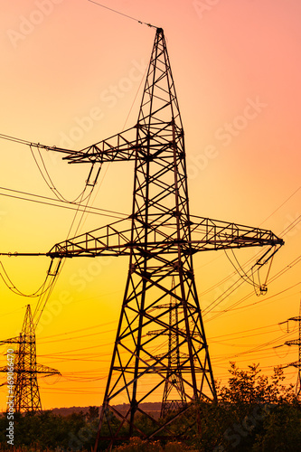 High-voltage power lines in the amazing pink and orange colors of sun dusk. Giantlike silhouette of an electricity pylon against the astonishing sunset backdrop.