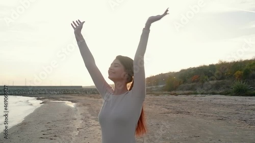 A young inspired girl raises her hands up, standing near the sea against the backdrop of a beautiful sunrise. Watching the sunset with a beautiful landscape