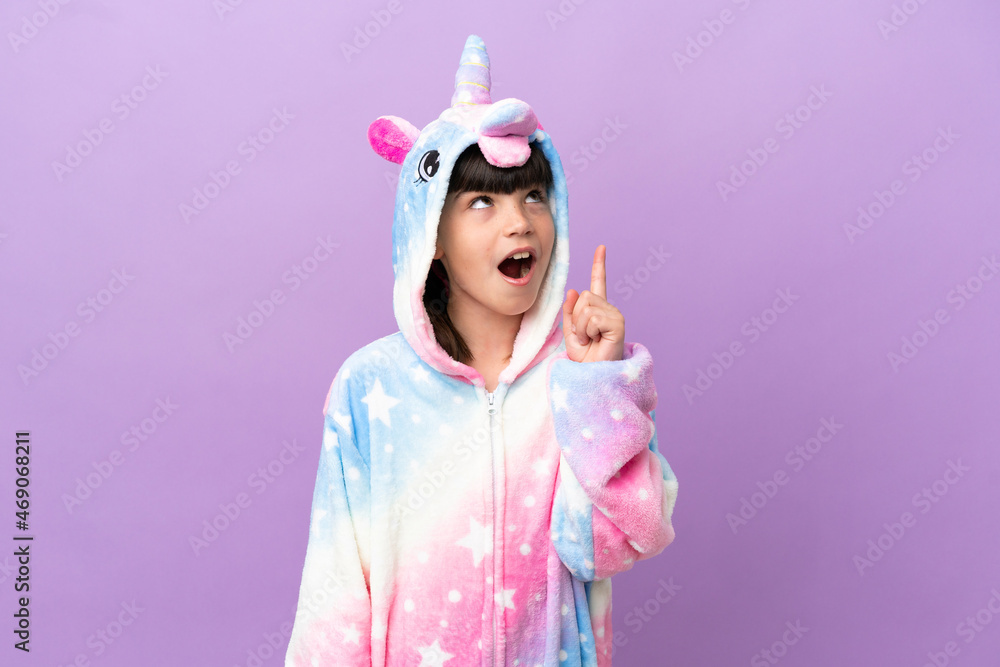 Little kid wearing a unicorn pajama isolated on purple background thinking an idea pointing the finger up Little kid wearing a unicorn pajama isolated on purple background thinking an idea pointing the finger up