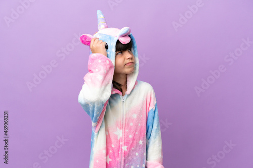 Little kid wearing a unicorn pajama isolated on purple background having doubts and with confuse face expression