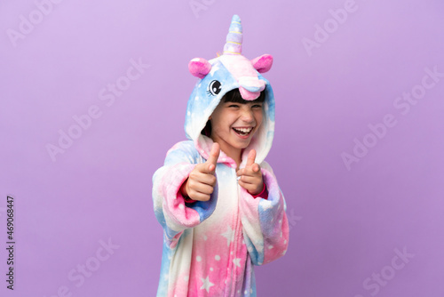 Little kid wearing a unicorn pajama isolated on purple background pointing to the front and smiling photo