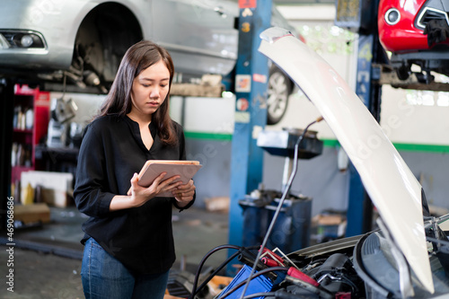Asian young woman holding a tablet on her hand and inspecting an old vehicle battery.
