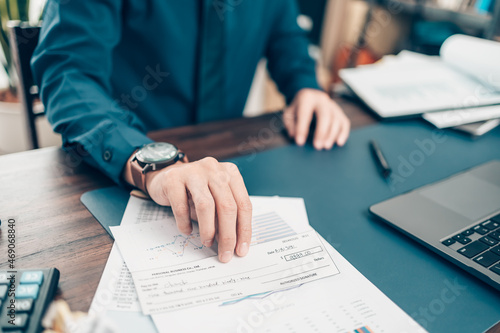 A Businessperson's hand giving cheque to customer and dollar bill, coin, laptop and graph chart on the desk at office. Payment by check, paycheck, payroll concept. photo