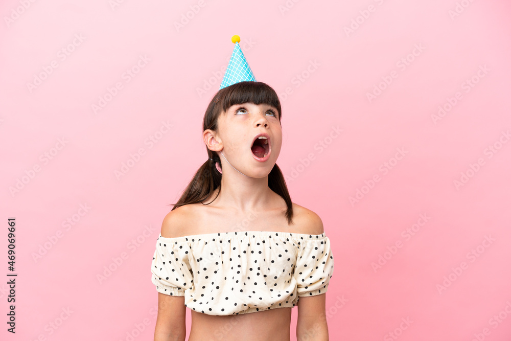 Little caucasian kid with birthday hat isolated on pink background looking up and with surprised expression Little caucasian kid with birthday hat isolated on pink background looking up and with surprised expression