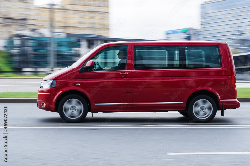 Fast moving Volkswagen Transporter T5 on the city road. Red VW multivan  riding on street. Commercial auto in fast motion with blurred background.  Stock Photo