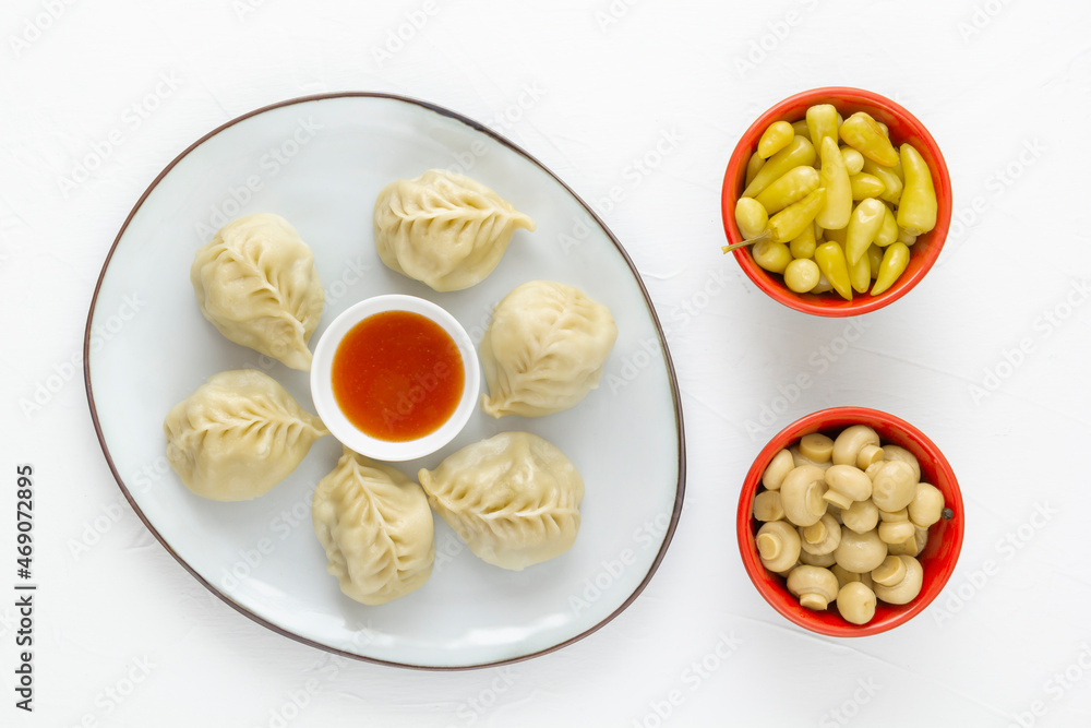 Boiled dumplings, manti or wontons with minced meat in a plate with sauce on a white table along with pickled mushrooms and hot peppers. Homemade food. View from above