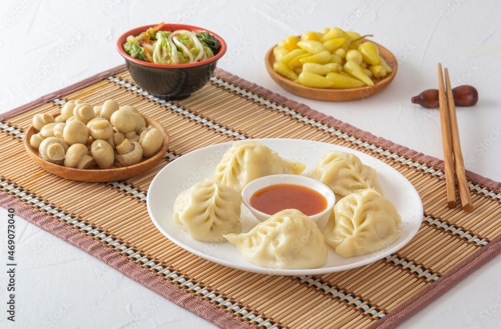Boiled dumplings, manti or minced wontons in a bowl of sauce on a straw mat along with chopsticks, pickled mushrooms, cabbage salad and hot peppers. homemade food Boiled dumplings, manti or minced wontons in a bowl of sauce on a straw mat along with chopsticks, pickled mushrooms, cabbage salad and hot peppers. homemade food