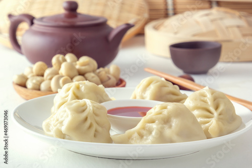 Boiled dumplings, manti or wontons with minced meat in a plate with sauce on a white table along with chopsticks and pickled mushrooms on the background of a kettle and a double boiler. homemade food