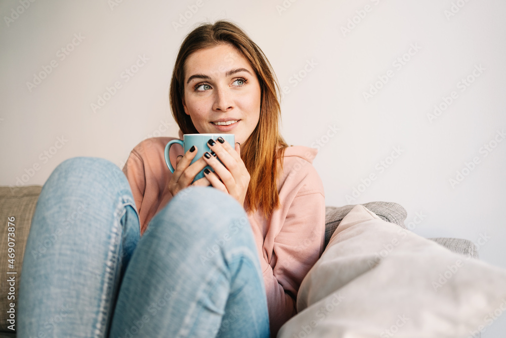 Pensive young woman sitting on a couch daydreaming