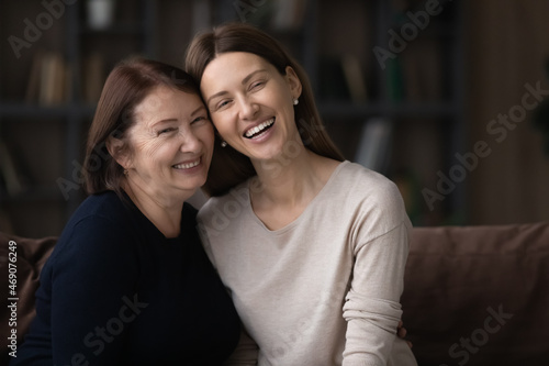 Happy mature woman with grownup daughter hugging sitting on couch, smiling young woman and senior mom spending leisure time together, having fun enjoying weekend, two generations good relationship