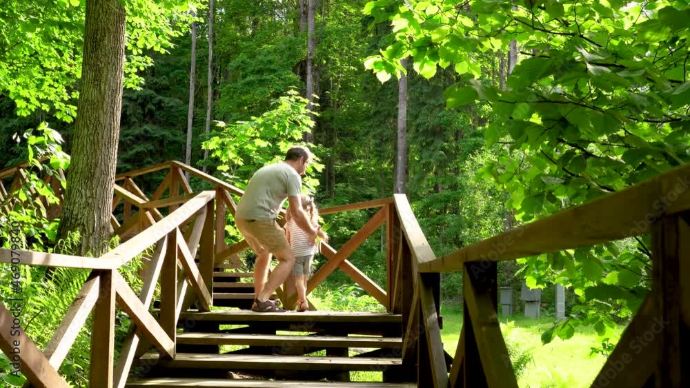 Dad put his daughter on his shoulders and tells stories about animals. Family vacation in the woods. Father's day concept. Family travel with children. Hiking trail with wooden deck in a forest. High