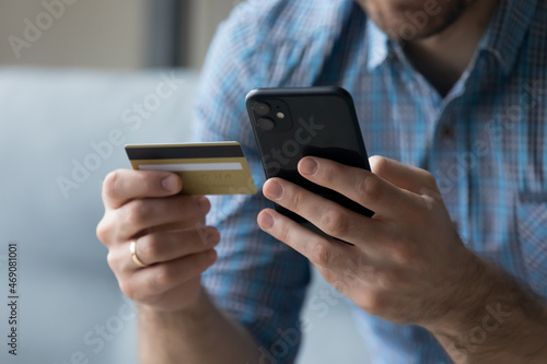 Close up young man holding cellphone and bank credit card in hands, purchasing goods and services online, satisfied with successful financial operation, secure shopping, wireless payment concept.