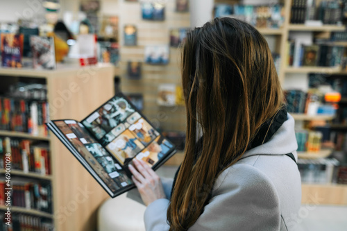 A beautiful young woman chooses a comic book for a gift in a bookstore to buy it. Woman stands with her back, comic book is open, blured.