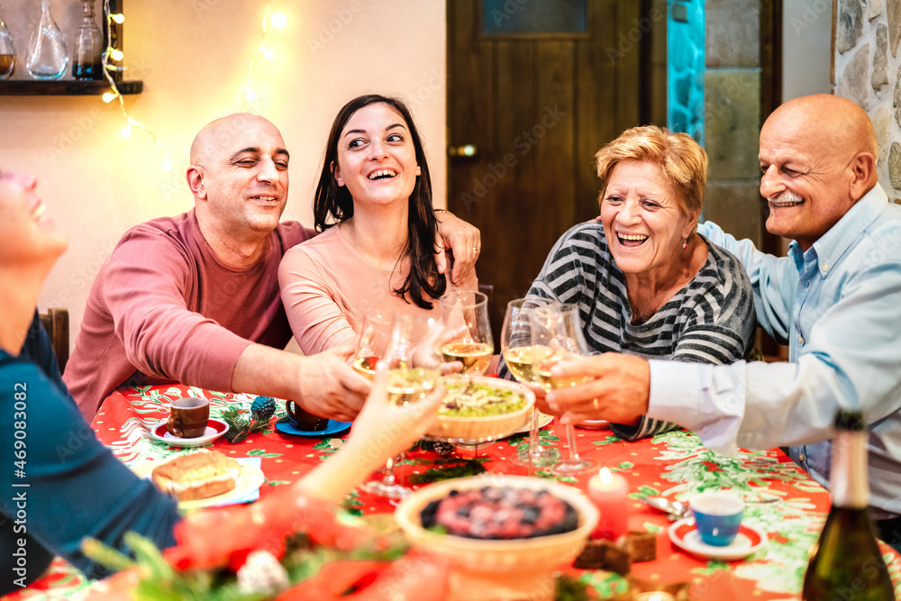 Mixed age group toasting white wine and having fun at winter holiday reunion - Dinner celebration concept with happy adult friends sharing time together at home party - Warm filter with focus on faces