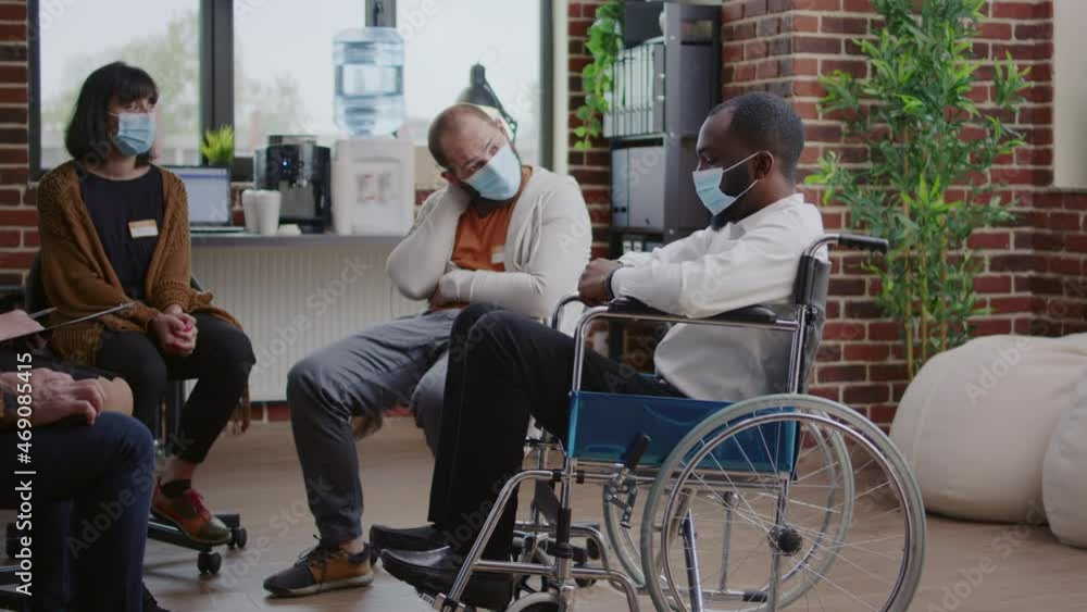 African american man with disability attending aa group therapy during coronavirus pandemic. Adult with face mask sitting in wheelchair while discussing alcohol addiction at rehab. African american man with disability attending aa group therapy during coronavirus pandemic. Adult with face mask sitting in wheelchair while discussing alcohol addiction at rehab.