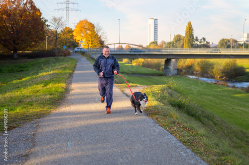Fototapeta Naklejka Na Ścianę i Meble -  Smiling man running his dog along a footpath at sunset