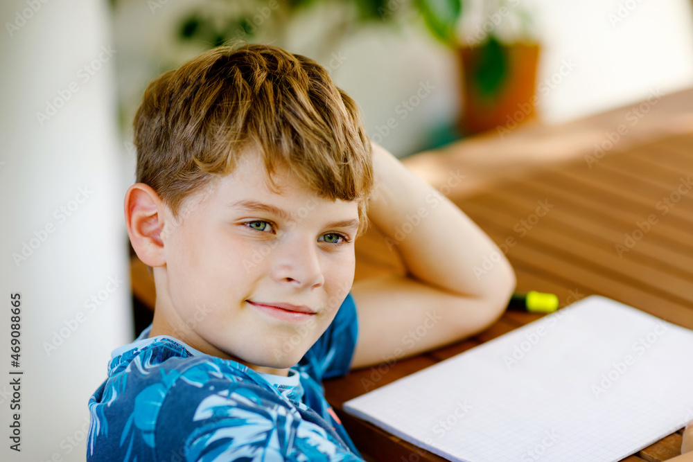 Hard-working happy school kid boy making homework during quarantine time from corona pandemic disease. Healthy child writing with pen, staying at home. Homeschooling concept Hard-working happy school kid boy making homework during quarantine time from corona pandemic disease. Healthy child writing with pen, staying at home. Homeschooling concept
