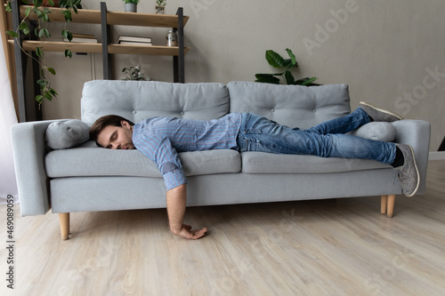 Fotografie Exhausted young man fell asleep on comfortable couch in modern living room, having no energy after hard working day
