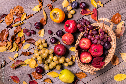 on a rustic wooden background a harvest of seasonal fruit and autumn colored dry leaves. photo