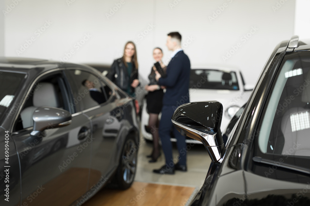 Auto business, car sales - a couple of friends of girls with a car dealer choose a car in a car dealership Auto business, car sales - a couple of friends of girls with a car dealer choose a car in a car dealership