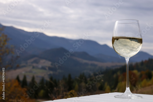 Glass of tasty wine on white wooden table against mountain landscape. Space for text