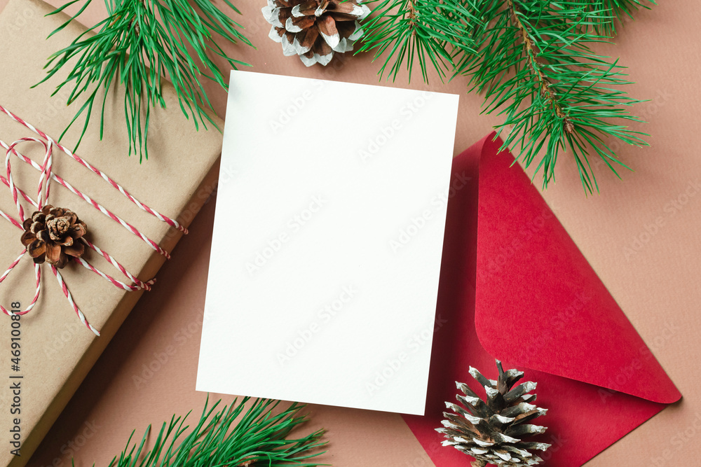 Christmas or New Year greeting card mockup with gift box, red envelope and pine tree branches with cones Christmas or New Year greeting card mockup with gift box, red envelope and pine tree branches with cones