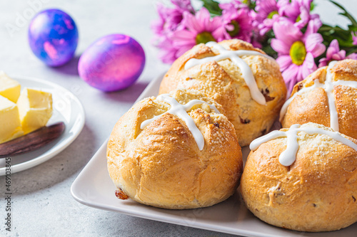 Traditional Easter cross buns with raisins on gray background with flowers and colored eggs.