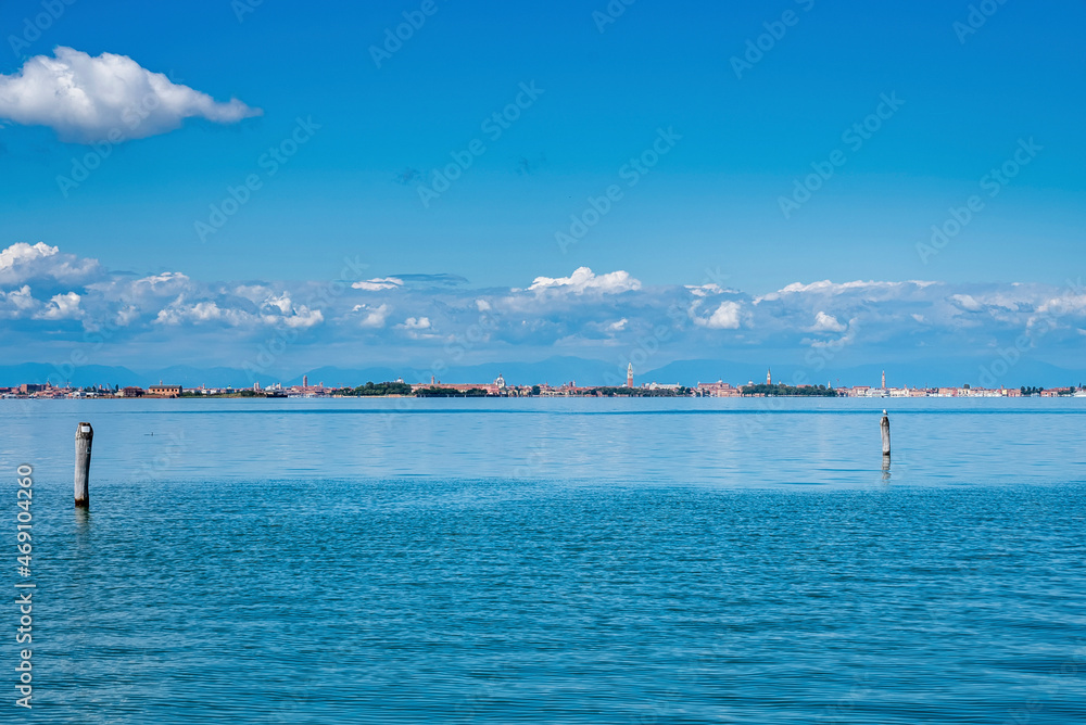Scenic view of beautiful sea water surface with wooden post along with plants and city buildings in the background