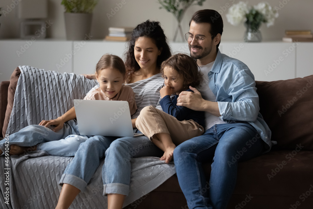 Happy parents with kids using laptop at home together, sitting on cozy couch, smiling mother and father with little son and daughter looking at computer screen, watching cartoons or movie, video call Happy parents with kids using laptop at home together, sitting on cozy couch, smiling mother and father with little son and daughter looking at computer screen, watching cartoons or movie, video call