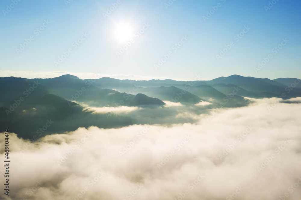 Aerial view of beautiful mountains covered with fluffy clouds on sunny day. Drone photography