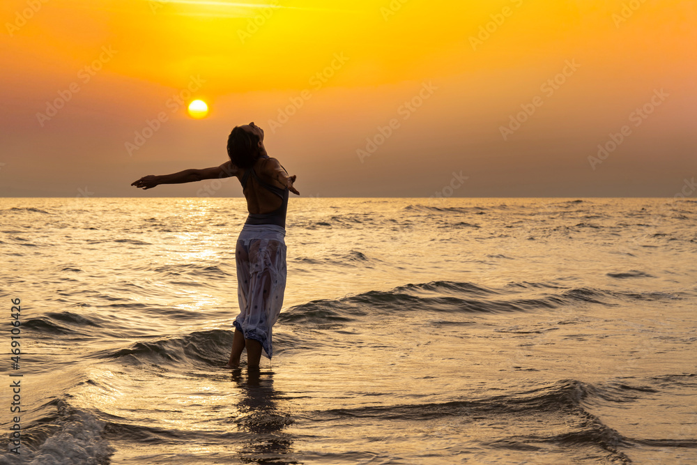 Beautiful woman in the sea with bathers clothes embraces the waist. The woman is dancing in the water with her arms outstretched. Copy space for your message.