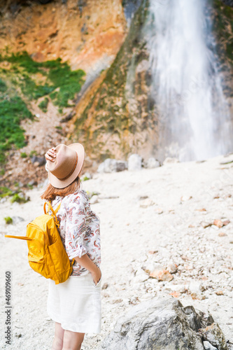 Young female traveler with yellow backpack and hat enjoying the view of Rinka waterfall in Logarska Valley. Traveling in Slovenia, Europe. Travel, wanderlust, freedom concept photo