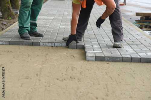 Builders lay concrete tiles on the sand in even rows, repair roads.