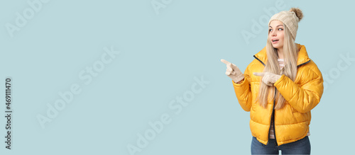 Beautiful young woman in winter clothes showing something on light background with space for text photo