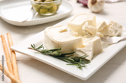Plate with crushed feta cheese on light wooden background