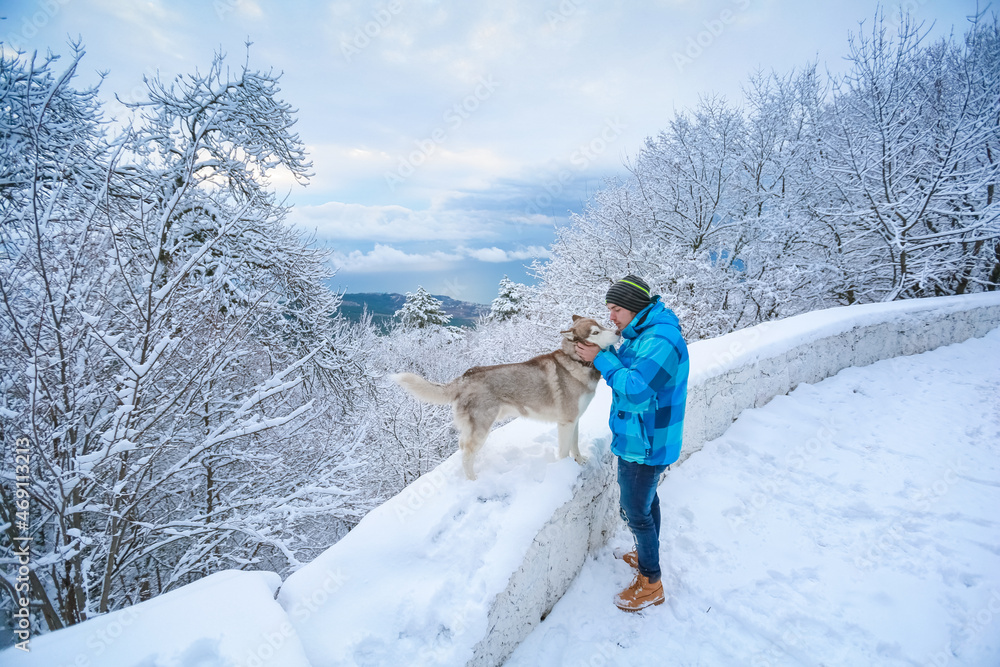 A man in warm clothes stands with a dog along a snowy mountain road