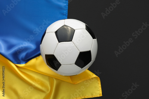 Ball for playing football and flag of Ukraine on black background