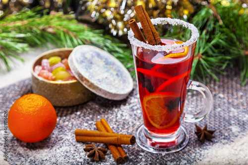 Christmas hot mulled wine with a slice of orange and spices. A glass cup with a hot traditional drink on a snowy background in festive decorations. Evening mood and decoration 