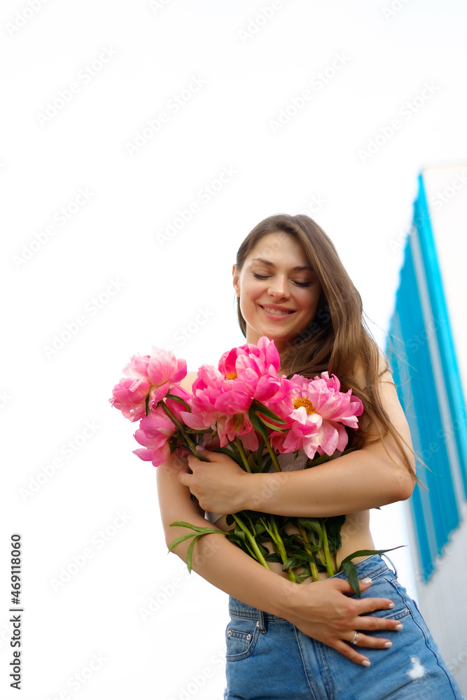 A young caucasian woman holding a bouquet of bright colors, a girl in denim shorts in summer with bunch of flowers , a lady in summer clothes against the sky A young caucasian woman holding a bouquet of bright colors, a girl in denim shorts in summer with bunch of flowers , a lady in summer clothes against the sky