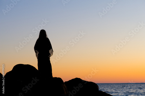 Silhouette of a woman on a rocky beach at sunset