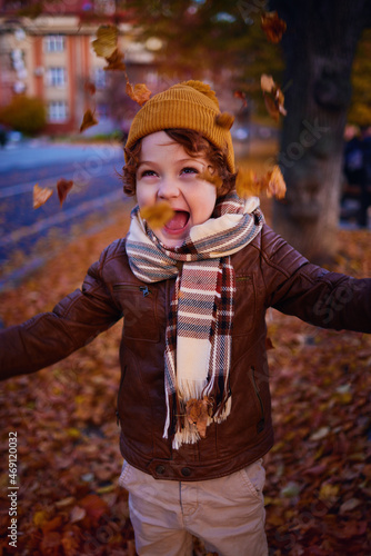 delighted young boy having fun on a walk in autumn city, throwing and catching fallen leaves