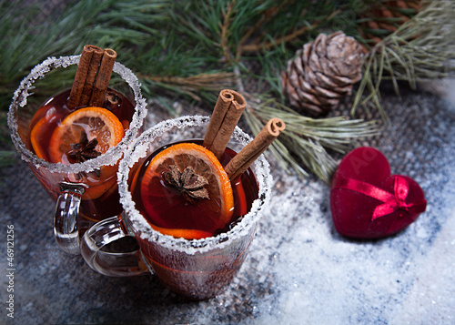 Christmas hot mulled wine with a slice of orange and spices. A glass cup with a hot traditional drink on a snowy background in festive decorations. Evening mood and decoration 