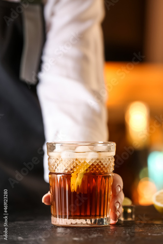 Female bartender with glass of tasty Cuba Libre cocktail on table in bar