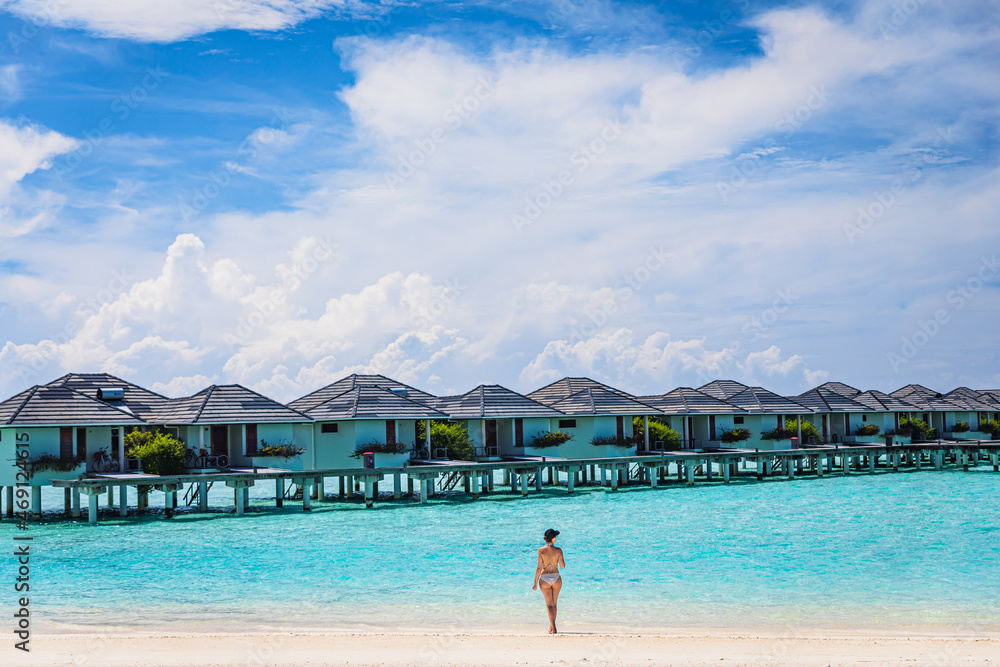 The girl stands in front of the water bungalows on a paradise island.